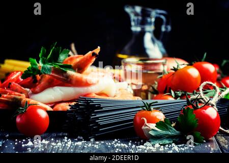 Spaghetti neri, pomodori ciliegini, vino bianco, gamberetti, calamari, vita morta in basso, fuoco selettivo Foto Stock