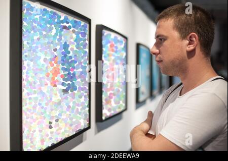Giovane uomo in galleria d'arte moderna che contempla opere d'arte. Pittura astratta Foto Stock