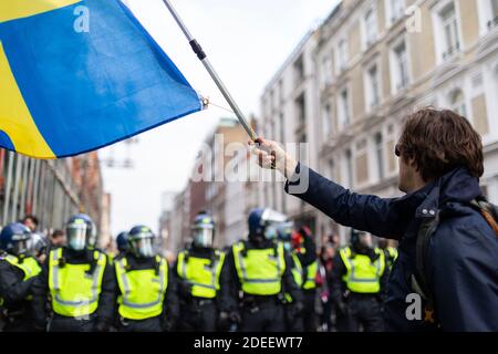 Protesta anti-lock-down, Londra, 28 novembre 2020. Un protetore ondeggia una bandiera di fronte a una fila di ufficiali di polizia in attrezzatura da rivolta. Foto Stock