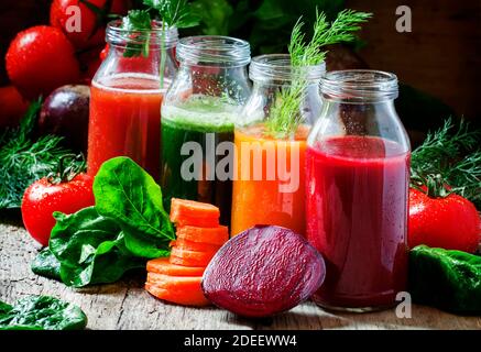 Quattro tipi di succhi di verdure: Rosso, borgogna, arancio, verde, in piccole bottiglie di vetro, verdure fresche ed erbe, sfondo di legno d'annata, selettivo Foto Stock