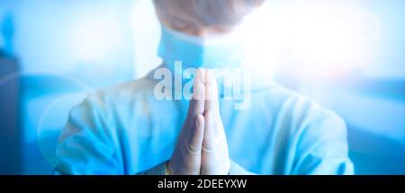 Giovane dottoressa che prega con le mani aggrappate insieme gesto, indossando maschera medica protettiva viso e uniforme blu. Primo piano con il lato di stampa rivolto verso l'alto Banner ampio con spazio per la copia. Salute, medicina e padella. Foto Stock