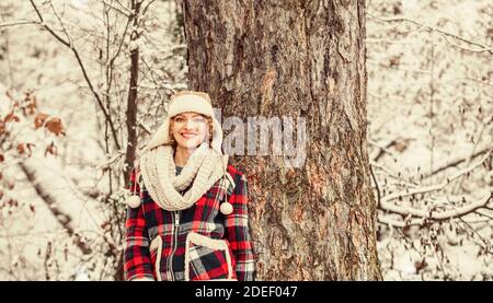 donna sorridente vicino all'albero. festa invernale giorno. donna carina in abiti caldi. Godersi la natura wintertime. Ritratto di donna eccitata in inverno. Ragazza allegra all'aperto relax. Giacca a scacchi donna. Foto Stock