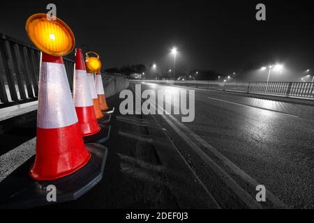 Coni stradali sul lato di una strada con i semafori in cima, Inghilterra UK. Foto grandangolare che mostra la prospettiva. Illustrazione, tema o concetto. Sicurezza stradale Foto Stock