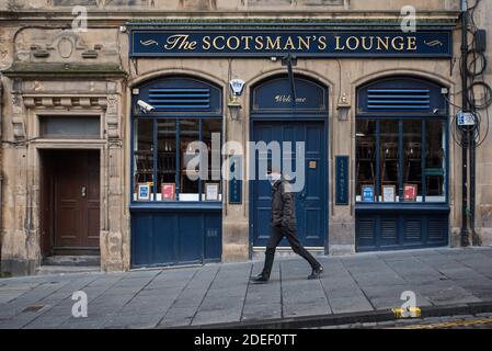 Uomo con una maschera a piedi davanti a una casa pubblica chiusa a causa delle restrizioni covid-19 a Edimburgo, Scozia, Regno Unito. Foto Stock