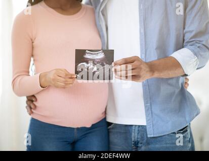 Vista ritagliata della giovane coppia incinta che tiene la foto del loro bambino non nato all'interno, primo piano Foto Stock