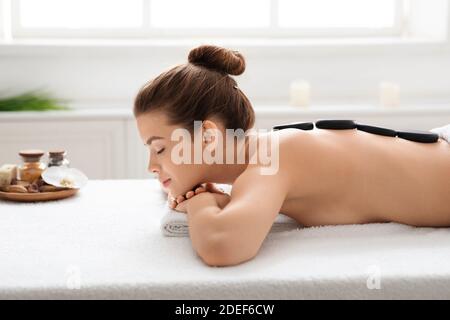 Vista laterale della giovane donna che riceve massaggio in pietra calda Foto Stock