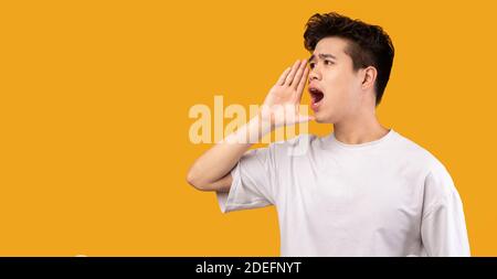 Uomo asiatico che tiene la mano vicino alla bocca, gridando da parte al copyspace Foto Stock