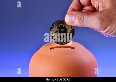 Terracotta piggy bank - scatola di denaro - isolato su sfondo blu. Salvataggio di un Bitcoin in un piggy-bank. Criptovaluta risparmio Foto Stock