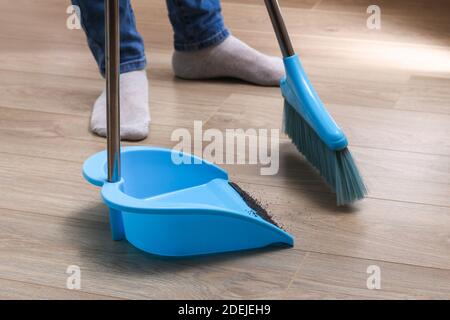 L'uomo spazza i detriti in una paletta blu con una spazzola. Foto Stock