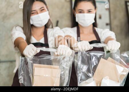 Primo piano cameriera indossare maschera protettiva sorriso e tenere la borsa per la spesa per portare via o take out cibo. Questo servizio essenziale è molto popolare mentre ci Foto Stock