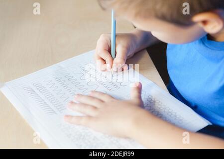 Capretto che fa la lezione a casa. Bambino ragazzo che scrive nel foglio di lavoro con la matita. Concetto di educazione dei bambini Foto Stock