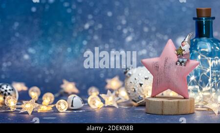 sfondo di natale con gnome di noel seduto su stella di legno contro sfondo blu sfocato con luci di vacanza incandescenti Foto Stock