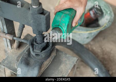 primo piano della mano del riparatore degli pneumatici quando si versa il carburante una pressa tradizionale quando si accatacciano uno pneumatico della motocicletta Foto Stock