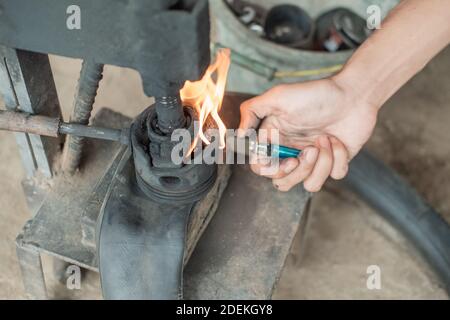primo piano della mano del riparatore di pneumatici quando si avvia un incendio con un accendisigari su una pressa tradizionale quando si accoppia un pneumatico per motocicletta Foto Stock