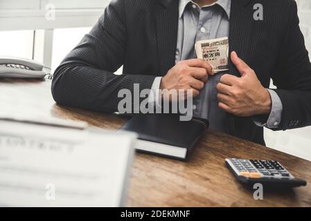 Uomo d'affari che tiene i soldi giapponesi dello yen nella tasca del vestito dopo la fabbricazione un affare in ufficio Foto Stock