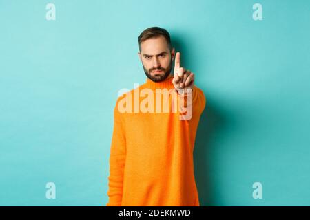 Uomo serio bearded accigliato, scuotendo il dito per proibire l'azione, proibire qualcosa, esprimere delusione, in disaccordo con voi, in piedi su azzurro chiaro Foto Stock