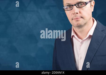 uomo di mezza età in occhiali alla moda su sfondo blu con figure astratte sfocate. Felice uomo di mezza età con occhiali guardando la macchina fotografica con p. Foto Stock