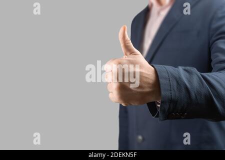 Mano di uomo d'affari che dà pollici su isolato su sfondo grigio. Primo piano gesturing mano OK isolato su bianco. Uomo d'affari con pollice su dorso grigio Foto Stock