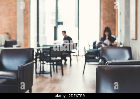 Vista offuscata dell'interno del caffè con sedie vuote di colore marrone scuro e pochi clienti si sono seduti a distanza contro una luce brillante all'esterno Foto Stock