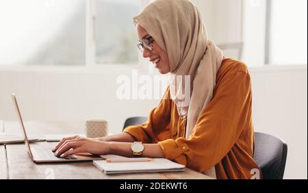 Donna che indossa hijab che lavora su un computer portatile a casa. Donna che lavora da casa utilizzando un computer portatile e sorridente. Foto Stock