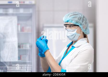 un infermiere in ospedale, che indossa una maschera protettiva e occhiali, contiene una siringa con medicinale. Medicina e assistenza sanitaria. Vaccinazione contro il coronavirus. Foto Stock