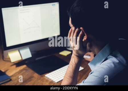 Uomo stanco e annoiato che lavora sul computer desktop di notte lavoro straordinario per completare il suo progetto Foto Stock