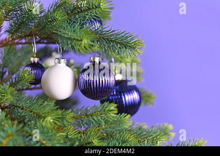 Baubles decorativi in vetro viola e bianco appesi all'albero di Natale diramazione su sfondo viola con spazio di copia Foto Stock