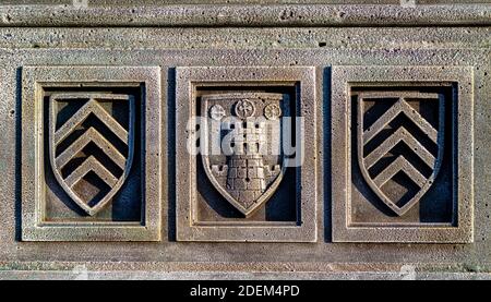 un frammento di una recinzione in pietra, un elemento decorativo con un'immagine in rilievo di tre scudi, uno dei quali raffigura una torre Foto Stock