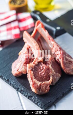 Tagliate a fette le costolette di agnello crudo su un tagliere di pietra Foto Stock