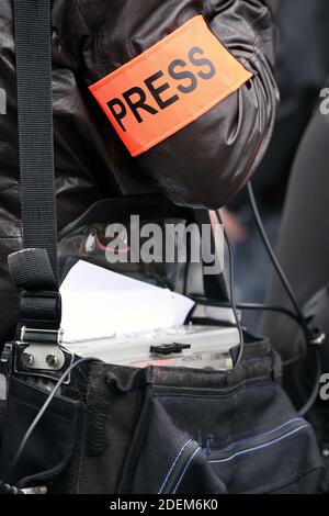 un giornalista che indossa un bracciale arancione ad alta visibilità con la scritta "PRESSE" e porta un dispositivo di registrazione audio portatile durante una manifestazione pubblica a Parigi Foto Stock