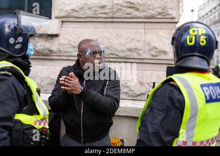 Protesta anti-lock-down, Londra, 28 novembre 2020. Un uomo nero che indossa uno scudo facciale si scontra con gli agenti di polizia in caschi di rivolta. Foto Stock