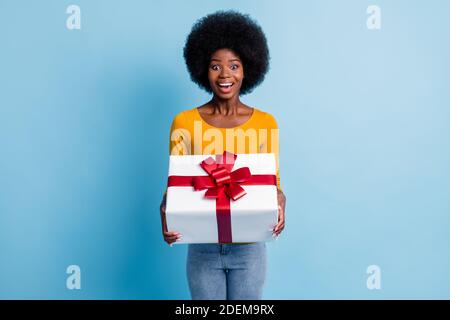 Ritratto fotografico di sorprendo sorridente donna nera con pelle che si avvolge con nastro regalo rosso isolato su sfondo di colore blu brillante Foto Stock