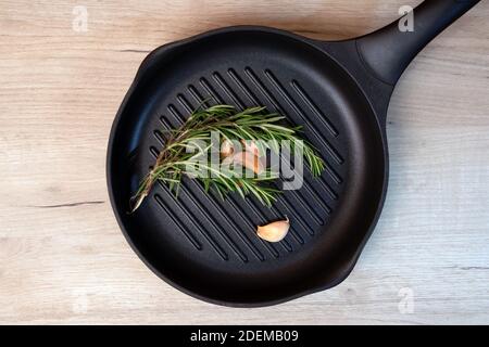 Padella nera su tavola di legno con rametti di rosmarino e spicchi d'aglio all'interno Foto Stock