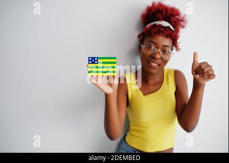 Donna brasiliana con i capelli afro tenere Goias bandiera isolata su sfondo bianco, mostrare il pollice in su. Concetto di Stati del Brasile. Foto Stock