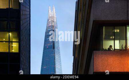 Vista attraverso la finestra dell'ufficio del lavoratore al suo computer con lo Shard in background, come visto da Lower Thames Street, Londra, marzo 2020 Foto Stock