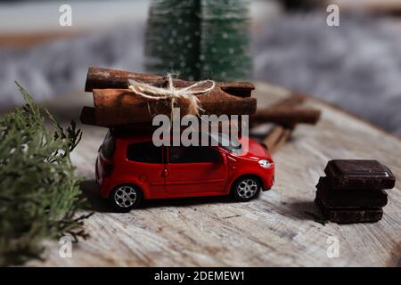 NIS, Serbia - 29 novembre 2020 Auto giocattolo rossa con un mazzo di bastoni di cannella sul tetto e cubetti di cioccolato su un ceppo di legno Foto Stock