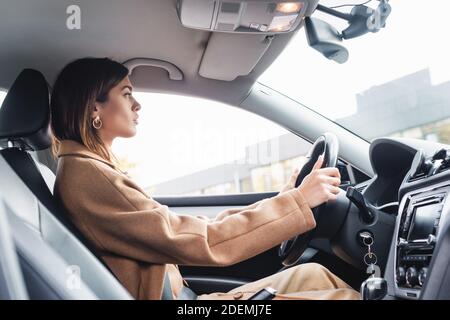 vista laterale della donna in trench coat che guida l'auto primo piano sfocato Foto Stock