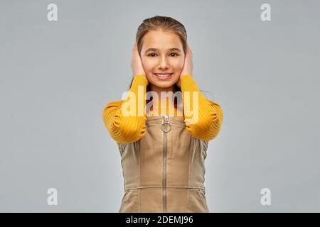 sorridente ragazza adolescente che chiude le orecchie con le mani Foto Stock