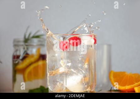 un pezzo di ghiaccio cade in un bicchiere, spruzzi cocktail di mirtillo rosso con ghiaccio e menta acqua detox con arancia, mirtillo e rosmarino, bevanda sana per il th Foto Stock