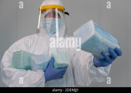 L'infermiere di sesso maschile indossa tuta protettiva con schermo facciale in plastica mostra una confezione di nuove maschere mediche durante una pandemia di covid-19 in un ospedale. Interno di Foto Stock