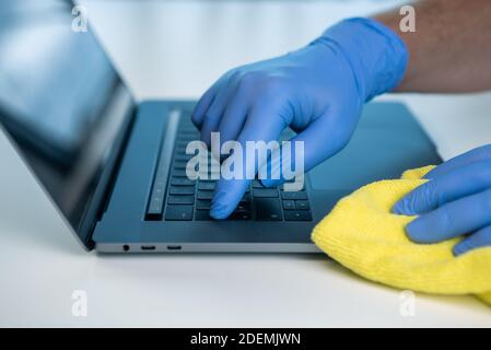 Un operatore sanitario strofinando il suo laptop con un panno per evitare la diffusione del coronavirus. Indossare guanti per pulire e disinfettare la tastiera del computer Foto Stock
