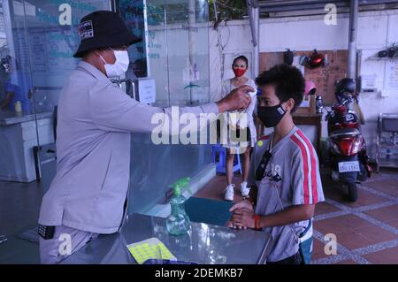 Un recente focolaio di COVID - 19 a Phnom Penh ha in corso test di massa. Un ragazzo di razza mista (cambogiano - americano), indossando una maschera protettiva viso / copertura, ottiene la sua temperatura controllata da una guardia di sicurezza all'ingresso di una clinica medica durante la pandemia coronavirus. Phnom Penh, Cambogia. 1° dicembre 2020. © Kraig Lieb Foto Stock