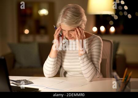 donna anziana che compila il modulo fiscale a casa in serata Foto Stock