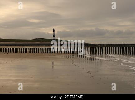 splendido paesaggio sulla costa della zelanda, nei paesi bassi, con la linea d'acqua sulla spiaggia di sabbia con una fila di frangiflutti e un faro tra le dune Foto Stock