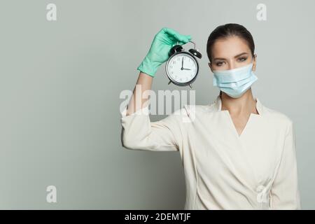 Donna medica seria in maschera medica protettiva e professionale sveglia con presa uniforme su sfondo bianco Foto Stock