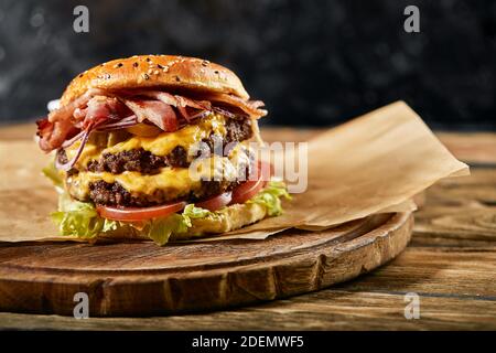 Un grande hamburger appetitoso con tortino di manzo alla griglia e verdure fresche. Gustoso cheeseburger americano su una tavola di legno. Hamburger classico fatto in casa Foto Stock