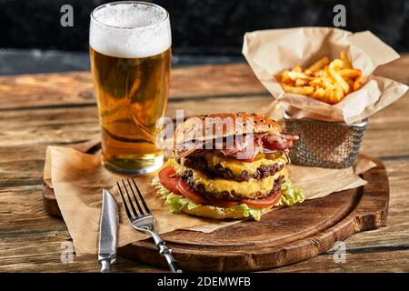 Un grande hamburger appetitoso con tortino di manzo alla griglia e verdure fresche. Gustoso cheeseburger americano su una tavola di legno. Hamburger classico fatto in casa Foto Stock