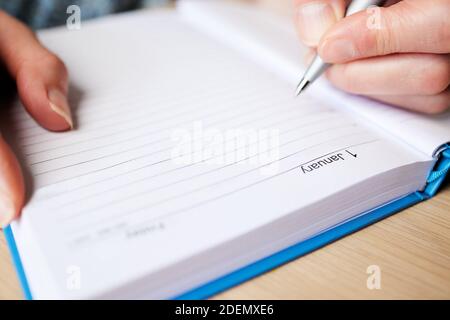 Primo piano di Woman Writing Resolution in New Year Diary Il 1 gennaio su tavolo a casa Foto Stock