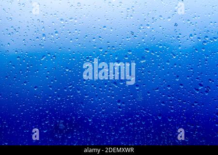 sfondo astratto, gocce di pioggia sul vetro contro il cielo blu tempesta Foto Stock