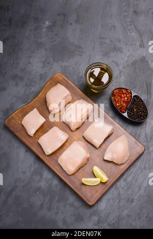 Pollo crudo tenero fritto senza pelle disposto su legno tavole e guarnite con olio, fette di limone, fiocchi freddi e pepe nero su sfondo grigio Foto Stock